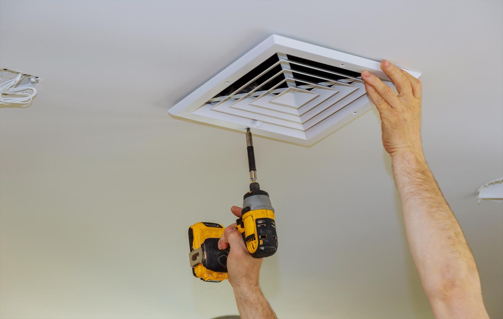 Hands removing a ceiling supply register with a cordless drill inside a home